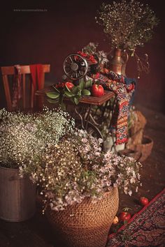 an arrangement of flowers and plants in baskets on a table with a chair behind them