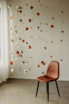 a chair sitting in front of a white wall with flowers hanging from it's sides