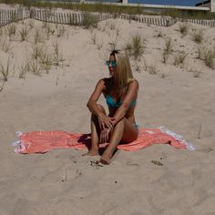 a woman sitting on top of a towel in the sand