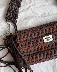 a brown and black woven purse with a tag on the front, sitting on a white sheet