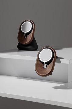 two wooden speakers sitting on top of a white shelf next to each other in front of a gray wall