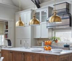 a kitchen with white cabinets and gold pendant lights hanging from the ceiling over the island