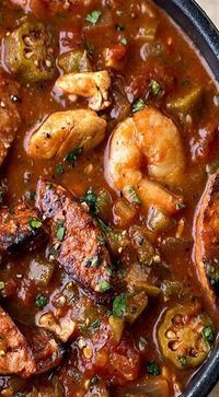 a black bowl filled with shrimp and vegetable stew on top of a wooden cutting board