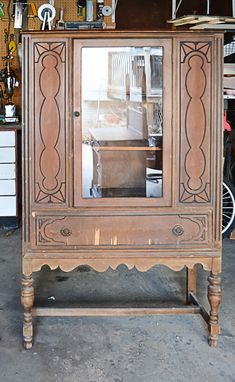 an old wooden cabinet with glass doors in a shop or repair shop, surrounded by tools and other items