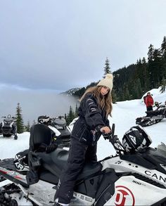 a woman standing on top of a snow covered slope next to skis and snowmobiles