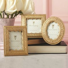 three gold frames sitting on top of a table next to a vase with white roses