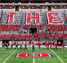 a group of people standing on top of a field next to a football stadium filled with fans