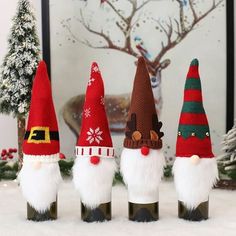 three wine bottles with gnome hats on them in front of a christmas tree and other decorations