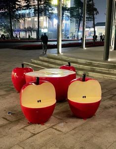 four apple shaped tables on the ground in front of some stairs at night with people walking by