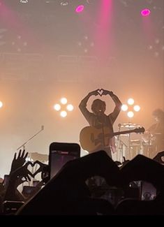 a man playing guitar on stage with his hands in the air while people are taking pictures