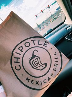 a chipotle bag sitting in the passenger seat of a car next to a steering wheel