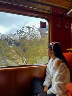 a woman sitting on a train looking out the window at snow covered mountains in the distance