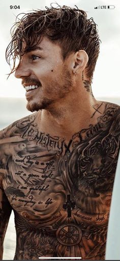 a man with tattoos on his chest standing next to the ocean and holding a surfboard