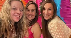 three women posing for the camera in front of colorful decorations