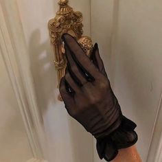 a woman's hand wearing black gloves and holding onto a gold door handle