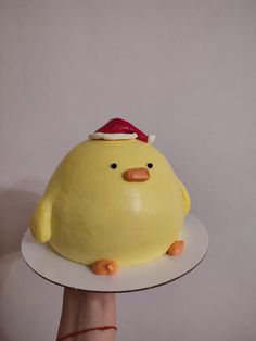 a hand holding a cake shaped like a yellow bird on top of a white plate