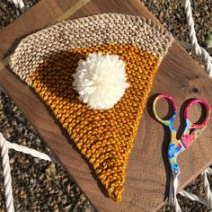 a knitted triangle with a white pom - pom sitting on top of it