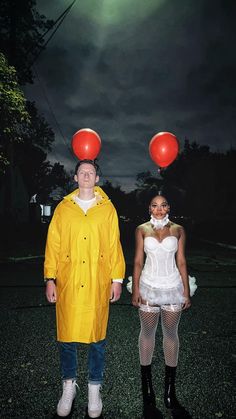 two people in raincoats standing next to each other with red balloons on their heads