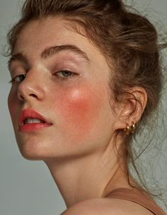 a woman with bright red makeup looks off to the side while she's wearing gold earrings