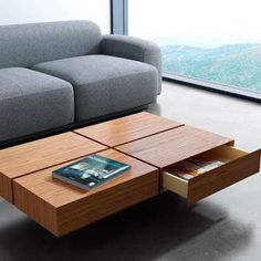 a couch and coffee table in front of a window with a book on the end