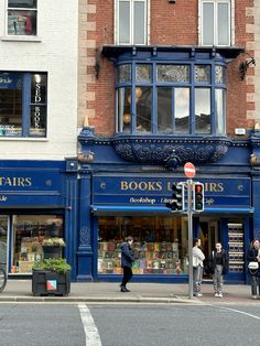 people are walking on the sidewalk in front of a book store with blue windows and shutters