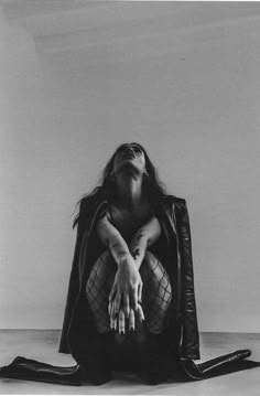 a black and white photo of a woman sitting on the floor with her hands up