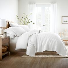 a bed with white comforters and pillows in a bedroom next to a window,