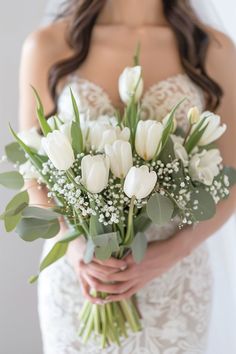 a bride holding a bouquet of white tulips and baby's breath flowers