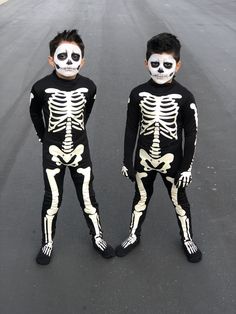 two young boys in skeleton costumes standing next to each other on the road with their faces painted white