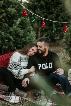 a man and woman sitting on a blanket in front of christmas trees