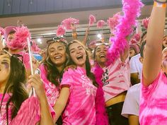 a group of young women in pink dresses and feathered hats cheer for the camera