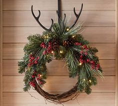 a christmas wreath hanging on the wall next to a door with lights and antlers