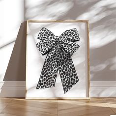 an animal print bow is hanging on the wall in front of a white framed art piece