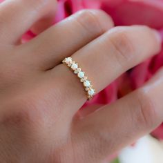 a woman's hand with a ring on it and pink flowers in the background