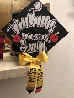 a graduation cap with the words teaching is a work of heart on it hanging from a mantle