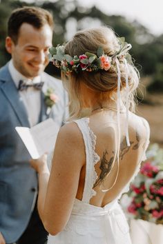 a bride and groom standing next to each other with tattoos on their back, looking at each other