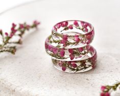 three rings with pink flowers on them sitting on a white surface next to some leaves