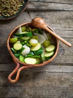 a wooden bowl filled with sliced cucumbers and other vegetables next to a spoon