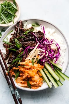 a white plate topped with meat and veggies next to chopsticks on top of rice