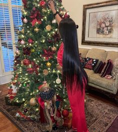 a woman decorating a christmas tree with red and gold ornaments on the bottom half