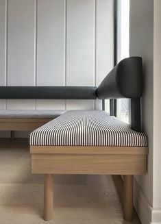 a bench with a striped seat cushion in front of a white wall and wooden floor