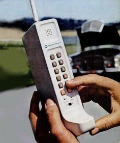 a hand holding a remote control in front of a parked car on the side of the road