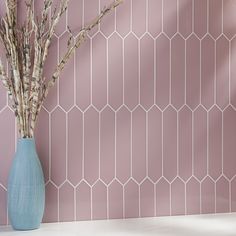 a vase filled with branches on top of a white counter next to a pink wall