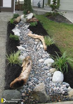 a small garden with rocks and plants in the center, along side a house that has grass on both sides