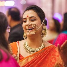 a woman in an orange and gold sari laughing with her face painted like a nose ring