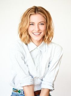 a woman with blonde hair wearing a white shirt and black pants smiling at the camera