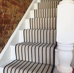 the stairs are lined with black and white striped carpet, along with a brick wall