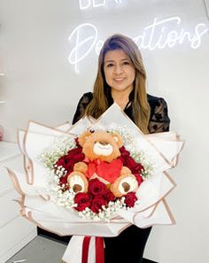 a woman holding a bouquet of roses and a teddy bear in front of a neon sign