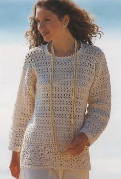 a woman standing on the beach wearing a white crochet sweater and matching necklace