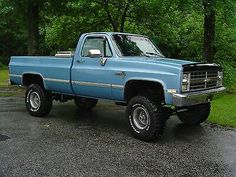 a blue pick up truck parked in a parking lot next to some green trees and grass